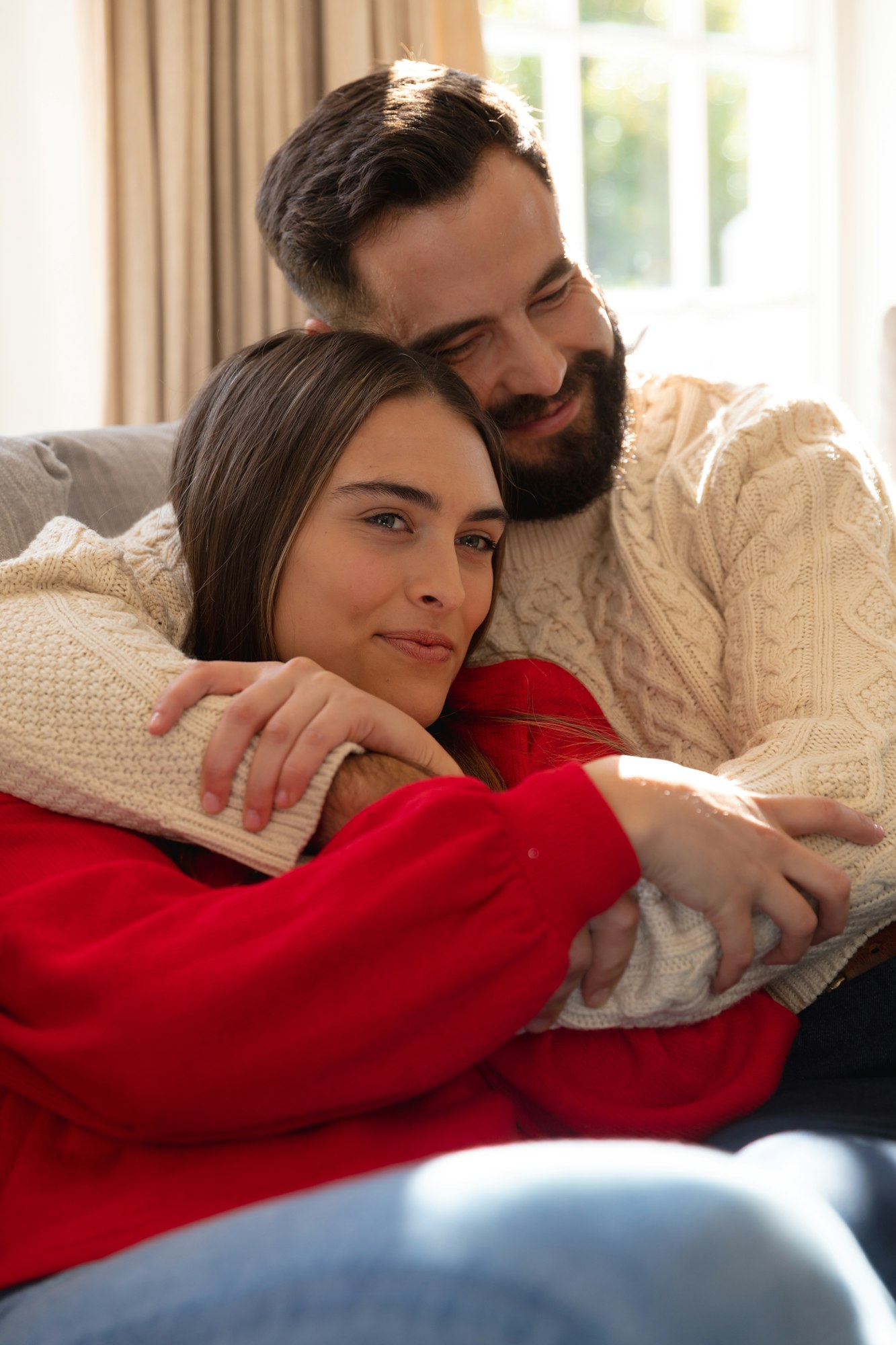 Happy caucasian couple sitting on couch in living room, smiling and embracing